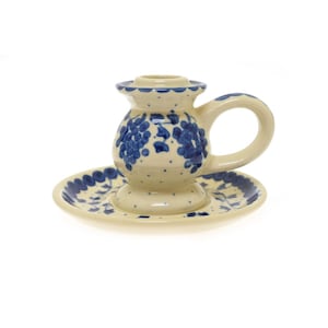 May include: A white ceramic candle holder with a blue grape design. The holder has a round base and a handle. It comes with a matching saucer.