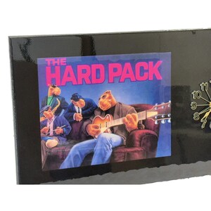 May include: Black rectangular clock featuring a graphic of a band of camels with the text "THE HARD PACK" on a blue background. The clock has a gold-colored clock face with black numbers and hands.