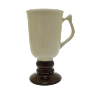 May include: A white ceramic mug with a brown pedestal base. The mug has a handle and a rounded shape.