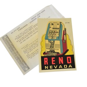 May include: A vintage-style sticker featuring a slot machine illustration in teal, red, and yellow, with the text "RENO NEVADA" in a black rectangle. The sticker is on a cream background, with a partially visible document behind it.