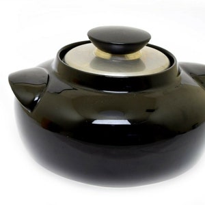 May include: A black ceramic crock pot with a silver lid and a black knob. The crock pot has two handles on the sides.