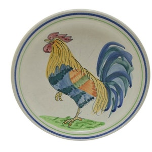 May include: A white ceramic plate with a blue, green, yellow, and red rooster design.