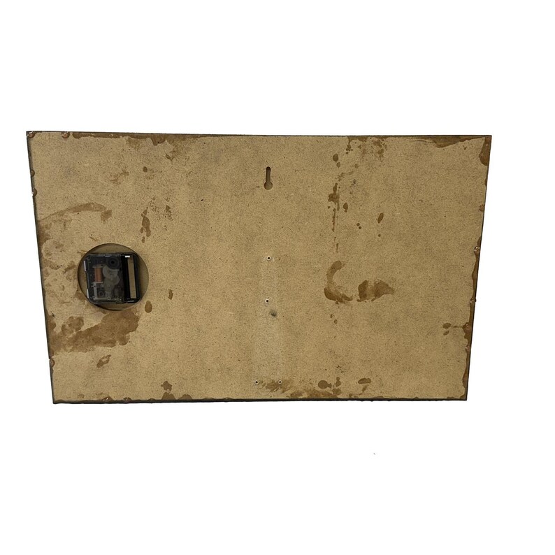 May include: The back of a rectangular clock with a clock mechanism on the left side. The clock's back is made of a light brown material with dark brown stains and a small hole for hanging.