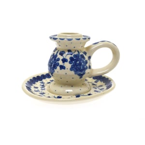 May include: A white ceramic candle holder with a blue and white grape design. The holder has a small plate base and a handle.