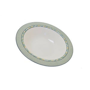 May include: A large, white ceramic bowl with a green and yellow floral design around the rim. The bowl is slightly tilted, showing the interior.