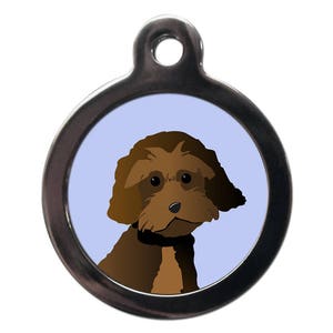 May include: A brown and white dog with curly hair is featured on a silver dog tag. The dog is looking at the camera with a friendly expression.