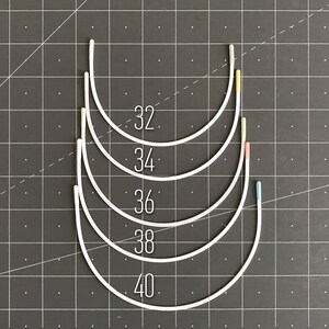 May include: Five white underwire bra bands in different sizes, labelled 32, 34, 36, 38, and 40. The bands are arranged in a stack, with the smallest size at the top and the largest size at the bottom.