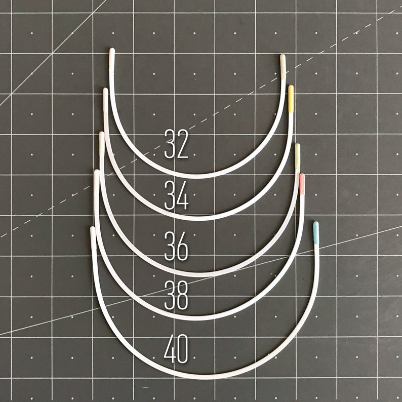 May include: Five white underwire bra bands in different sizes, labelled 32, 34, 36, 38, and 40. The bands are arranged in a stack, with the smallest size at the top and the largest size at the bottom.