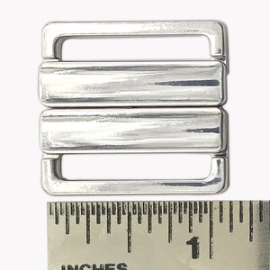 May include: Silver-toned metal bra strap slider with three rows of metal. The slider measures approximately 1 inch in length.