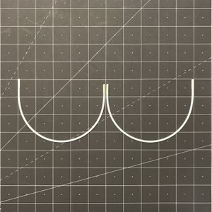 May include: Two white metal bra underwires, curved and joined at the centre, on a grey grid background.