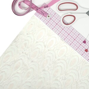 May include: A craft scene with white patterned fabric, a pink measuring tape, a clear ruler, and white scissors with pink accents. Two heart-shaped pins are also visible, suggesting a focus on sewing and design.