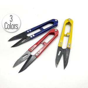 Peut inclure: Trois paires de petites ciseaux avec des poignées de couleurs différentes : bleu, rouge et jaune. Les ciseaux ont des lames noires et sont conçus pour couper le fil.