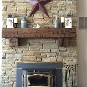 Puede incluir: Una chimenea de piedra r&uacute;stica con un manto de madera y una estufa de le&ntilde;a negra. La chimenea est&aacute; decorada con una estrella roja, velas y jarrones.