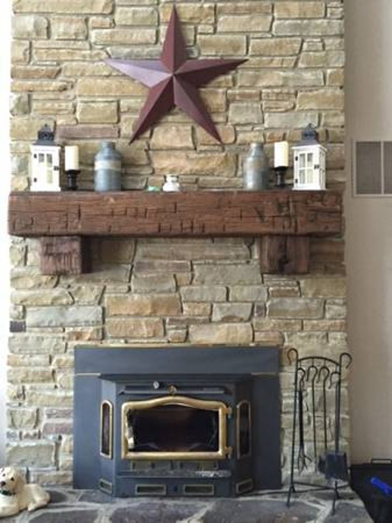 Puede incluir: Una chimenea de piedra r&uacute;stica con un manto de madera y una estufa de le&ntilde;a negra. La chimenea est&aacute; decorada con una estrella roja, velas y jarrones.