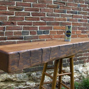 Puede incluir: Un estante de viga de madera r&uacute;stica con un acabado marr&oacute;n desgastado. El estante est&aacute; montado en un taburete de madera con un acabado marr&oacute;n. Una lata vintage de soda "Reading" est&aacute; sentada en el estante.