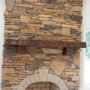 Puede incluir: Una chimenea de piedra con una repisa de madera r&uacute;stica y un hogar de ladrillo blanco. La chimenea est&aacute; construida con una variedad de piedras en tonos marrones, grises y beige.