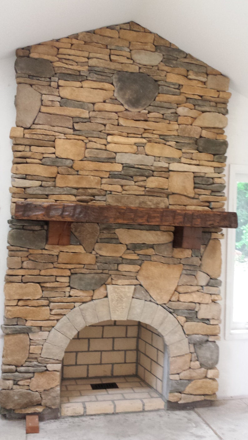 Puede incluir: Una chimenea de piedra con una repisa de madera r&uacute;stica y un hogar de ladrillo blanco. La chimenea est&aacute; construida con una variedad de piedras en tonos marrones, grises y beige.