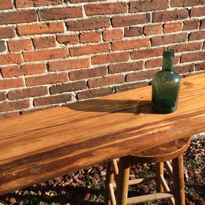 Puede incluir: Una larga barra de madera con una mancha marr&oacute;n oscura. La barra est&aacute; apoyada en una pared de ladrillo y tiene una botella de vidrio verde encima.