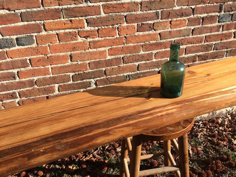Puede incluir: Una larga barra de madera con una mancha marr&oacute;n oscura. La barra est&aacute; apoyada en una pared de ladrillo y tiene una botella de vidrio verde encima.