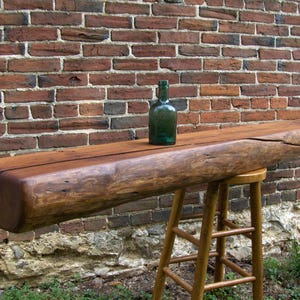 Puede incluir: Una repisa de madera r&uacute;stica para la chimenea con un acabado marr&oacute;n oscuro. La repisa est&aacute; hecha de madera recuperada y tiene un aspecto natural y desgastado. Una botella de vidrio verde est&aacute; sentada en la repisa.