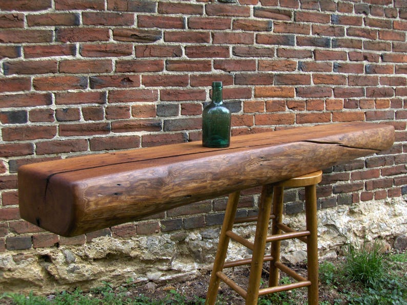 Puede incluir: Una repisa de madera r&uacute;stica para la chimenea con un acabado marr&oacute;n oscuro. La repisa est&aacute; hecha de madera recuperada y tiene un aspecto natural y desgastado. Una botella de vidrio verde est&aacute; sentada en la repisa.