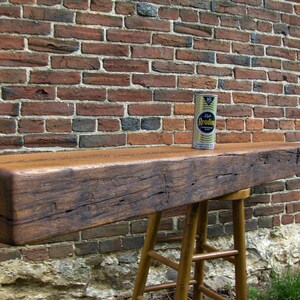 Puede incluir: Un estante de madera r&uacute;stico con un acabado marr&oacute;n desgastado, montado en una pared de ladrillo. El estante est&aacute; apoyado en un taburete de madera con un acabado marr&oacute;n claro. Una lata de abrillantador para muebles se encuentra en el estante.