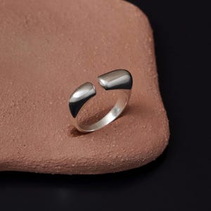 May include: A silver ring with a unique open design. The ring is made of smooth, polished metal and has a simple, modern aesthetic.