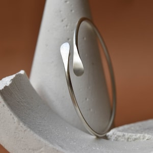 Peut inclure: Un bracelet jonc en argent avec un design incurvé unique. Le bracelet est fait d'une seule pièce de métal qui est pliée en cercle puis tordue à une extrémité pour créer une forme distinctive.