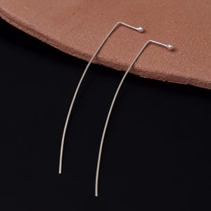 Può includere: Un paio di orecchini lunghi e sottili in argento con piccole sfere rotonde alle estremità.