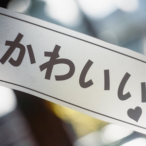 May include: A white card with the Japanese text "kawaii" written in black, surrounded by small black hearts.