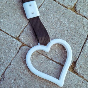 May include: White heart-shaped handle with a black strap. The strap has a white rectangular piece with two small holes.