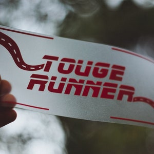 May include: White sticker with red text that says "Touge Runner" and a red winding road graphic.