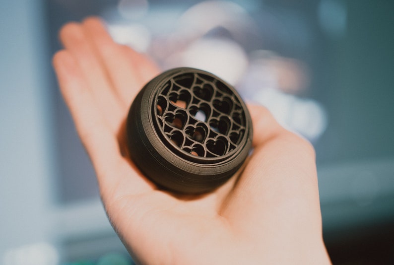 May include: A black, round, 3D printed object with a design of hearts cut out of the surface.