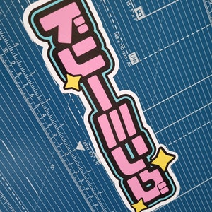 May include: A pink and black sticker with the text "Dreaming" in Japanese characters. The sticker has a blue outline and two yellow stars.