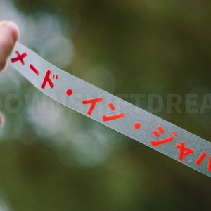 May include: A clear plastic strip with red Japanese characters that read "メード・イン・ジャパン" which translates to "Made in Japan".