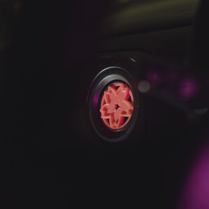 May include: Close-up of a black car air freshener with a pink cherry blossom design.