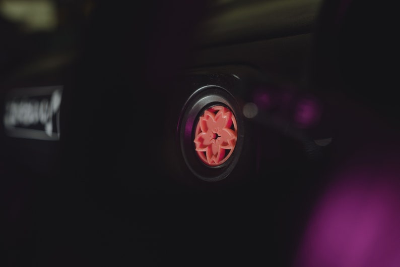 May include: Close-up of a black car air freshener with a pink cherry blossom design.