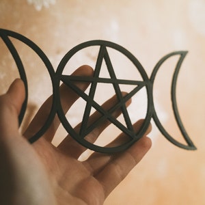 May include: A black metal pentagram with three crescent moons on either side. The pentagram is a five-pointed star with a circle around it.