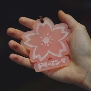 May include: A pink plastic charm shaped like a cherry blossom with the text "ドリーミン" (Dreamin) and "DOWNTOWN TURBANS" in white lettering.