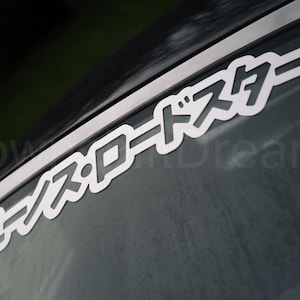 May include: A black car with a white vinyl sticker on the rear window that says "ユーノスロードスター".