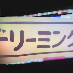 May include: A holographic sticker with the Japanese text "Dreaming" in white lettering with two small hearts on either side of the text.