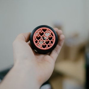 May include: A black and pink 3D printed object with a heart design. The object is being held in a person's hand.