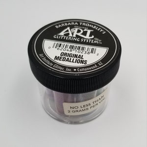 May include: A black jar with a white label that reads "Barbara Trombley's Original Art Glittering SystemTM". The label also includes a barcode, the text "Original Medallions", and "Art Institute Glitter, Inc. Cottonwood, AZ". The jar contains a clear plastic container with colorful glitter inside. The label on the jar reads "No Less Than 2 Grams Per Vial".