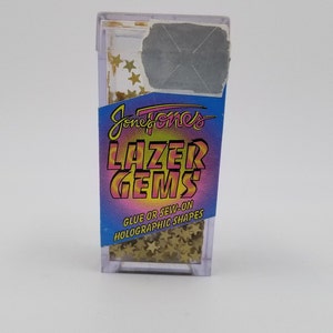 May include: A clear plastic container filled with gold star-shaped holographic gems. The container has a pink, blue, and yellow label that reads "Jone Jones Lazer Gems Glue or Sew-on Holographic Shapes".