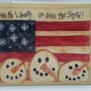 May include: A wooden sign with a painted American flag and three snowmen. The sign reads "Give Me Liberty... or Give Me Snow!"