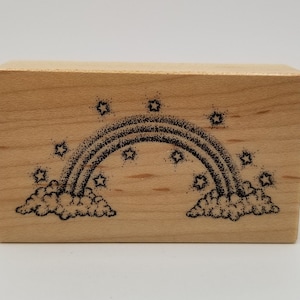 May include: A wooden stamp with a black and white illustration of a rainbow with stars and clouds.