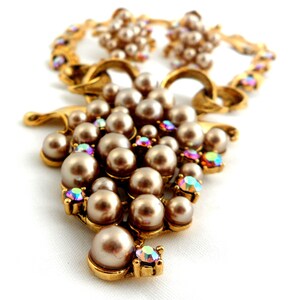 May include: A gold tone necklace and earrings set with a cluster of faux pearls and iridescent rhinestones. The necklace features a large cluster of pearls and rhinestones in the shape of a grape.