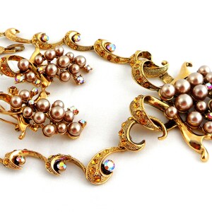May include: A gold-tone necklace and earrings set featuring a grape motif with faux pearls and iridescent rhinestones.