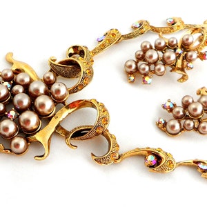 May include: A gold-tone necklace and earrings set featuring a grape motif with faux pearls and iridescent rhinestones.
