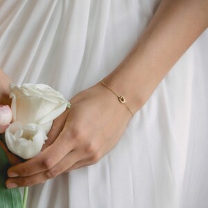 May include: A delicate gold chain bracelet with a small, circular pendant. The bracelet is worn on a person's wrist.